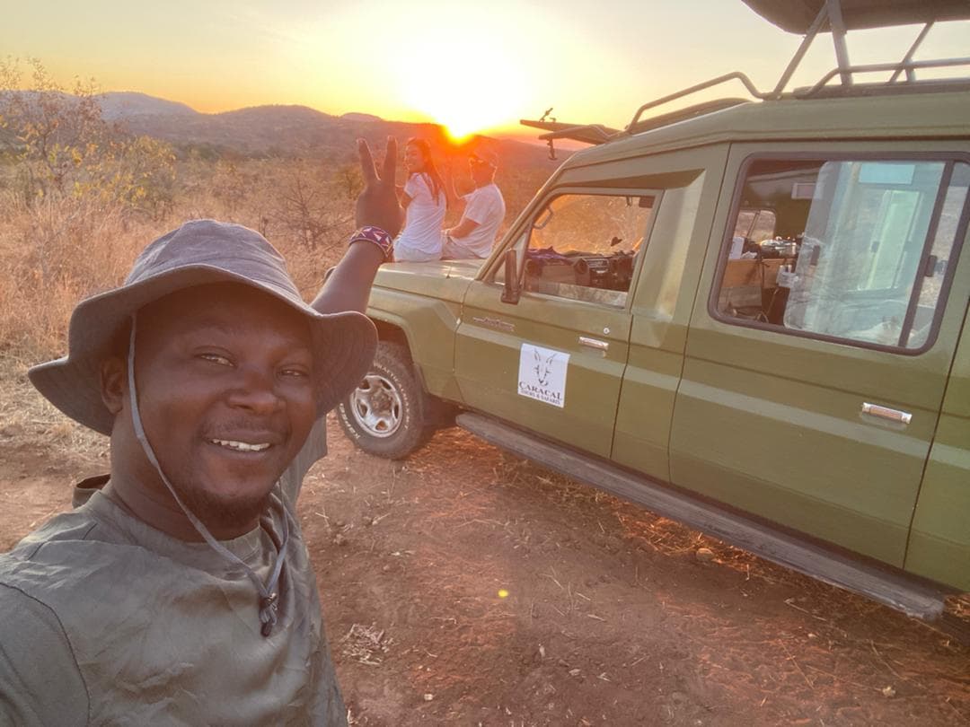 En guide tar en selfie vid safaribilen i solnedgången
