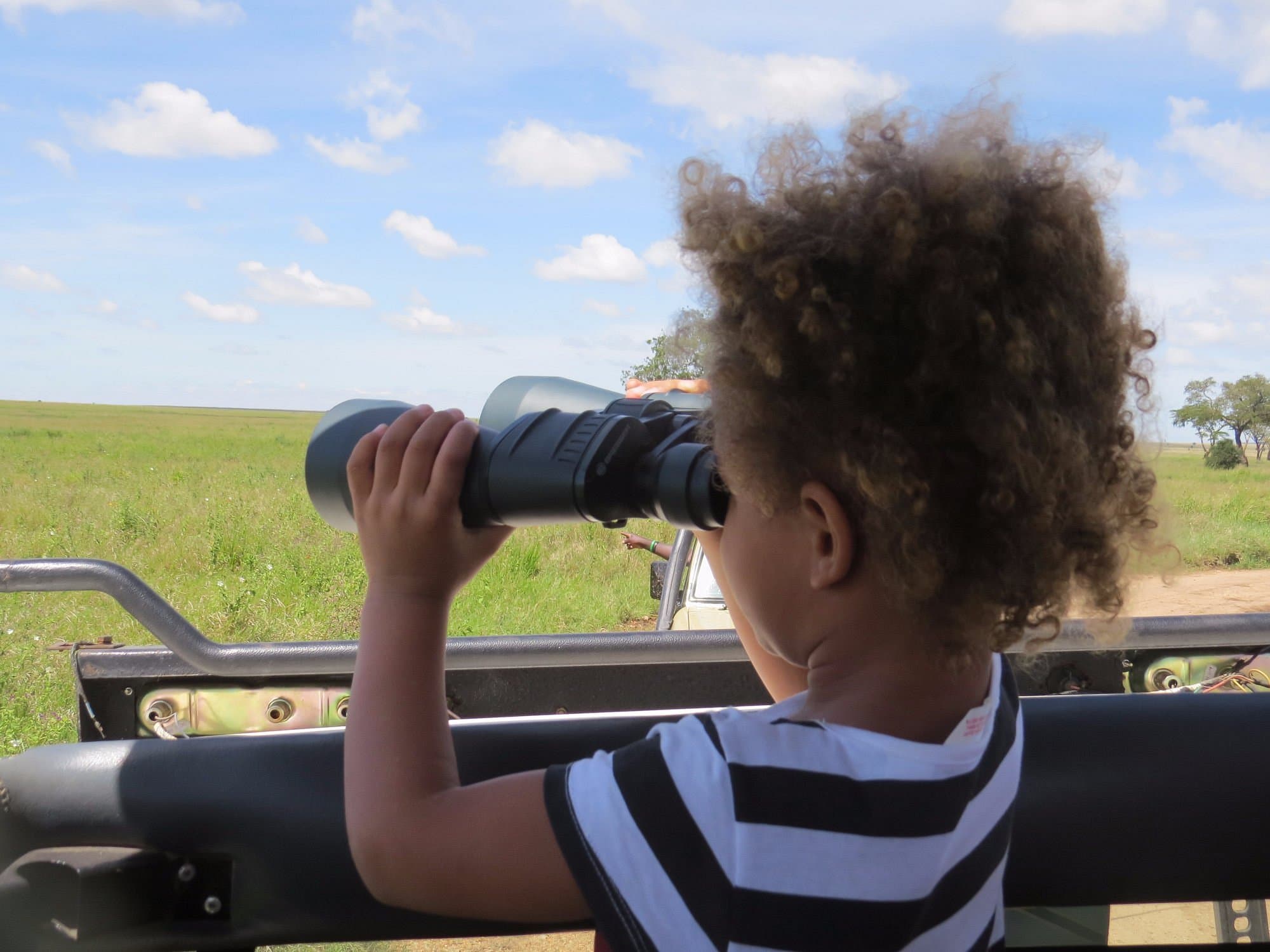 Ett barn spanar med kikare från safaribilen