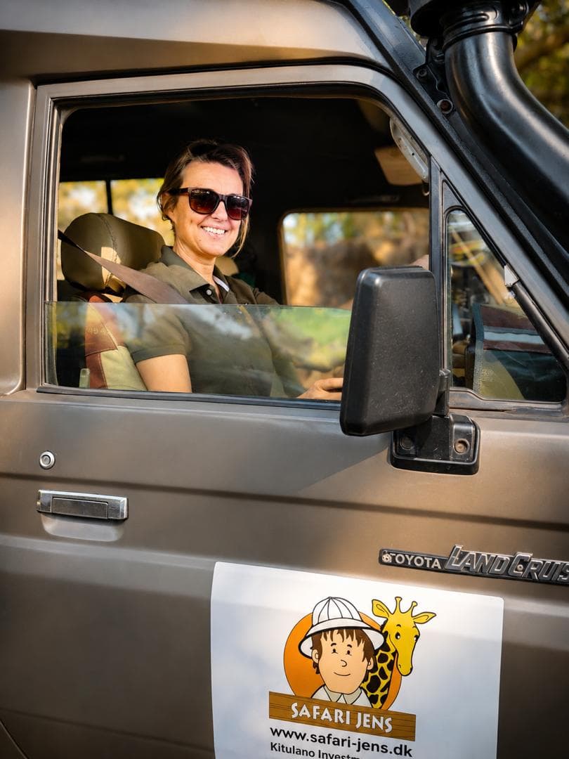 En leende resenär i förarsätet på en safaribil med Safari Jens logotyp